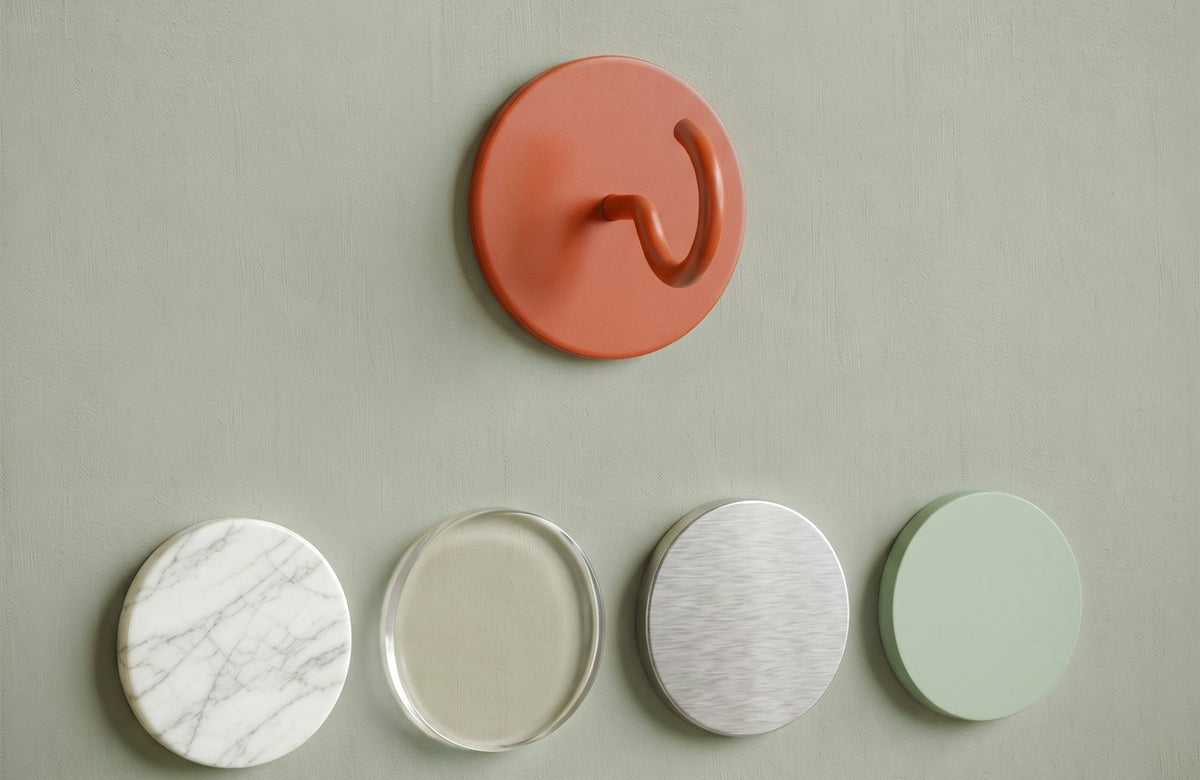 Runder Klebehaken an der Wand, darunter Muster von Marmorfliese, Glas, gebürstetem Metall und lackiertem Holz