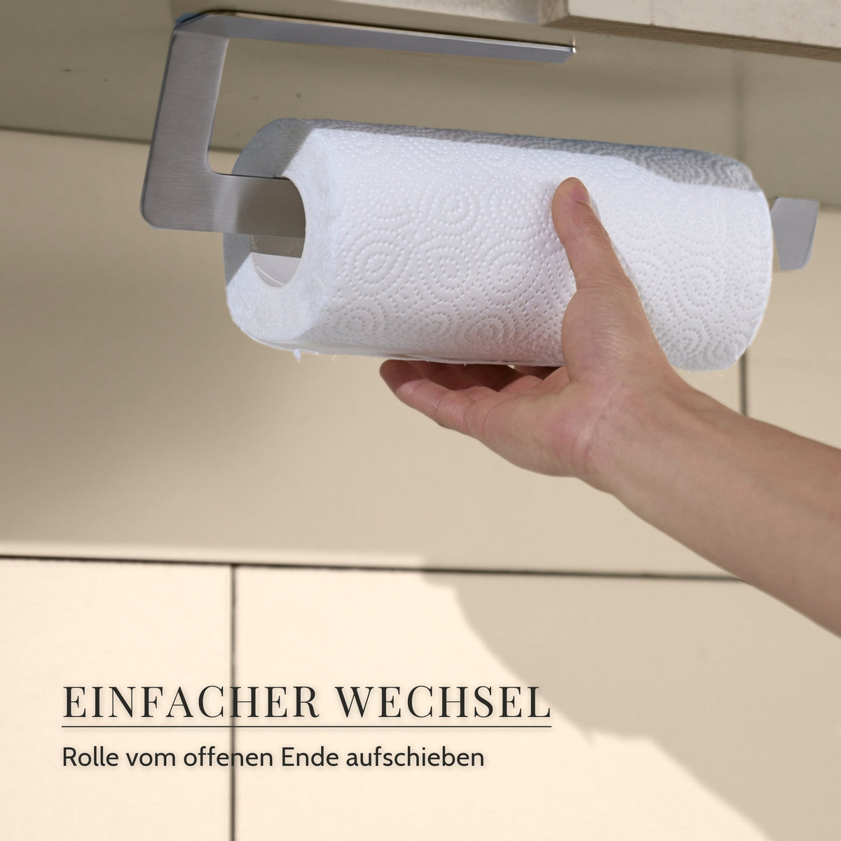 Hand schiebt eine Küchenrolle vom offenen Ende auf den Küchenrollenhalter aus gebürstetem Edelstahl unter dem Hängeschrank · Einfacher Wechsel: Rolle vom offenen Ende aufschieben