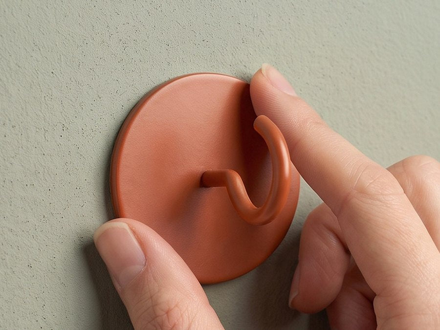 Finger drücken die Platte des Hakens fest an die Wand